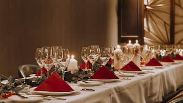 A long dining table set with multiple wine glasses, red napkins, and white plates, with candles and greenery.