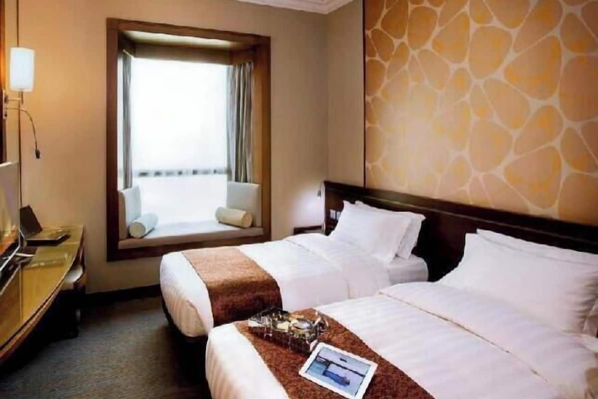 A hotel room with two beds, a desk, a lamp, a window with curtains, and a patterned wall.