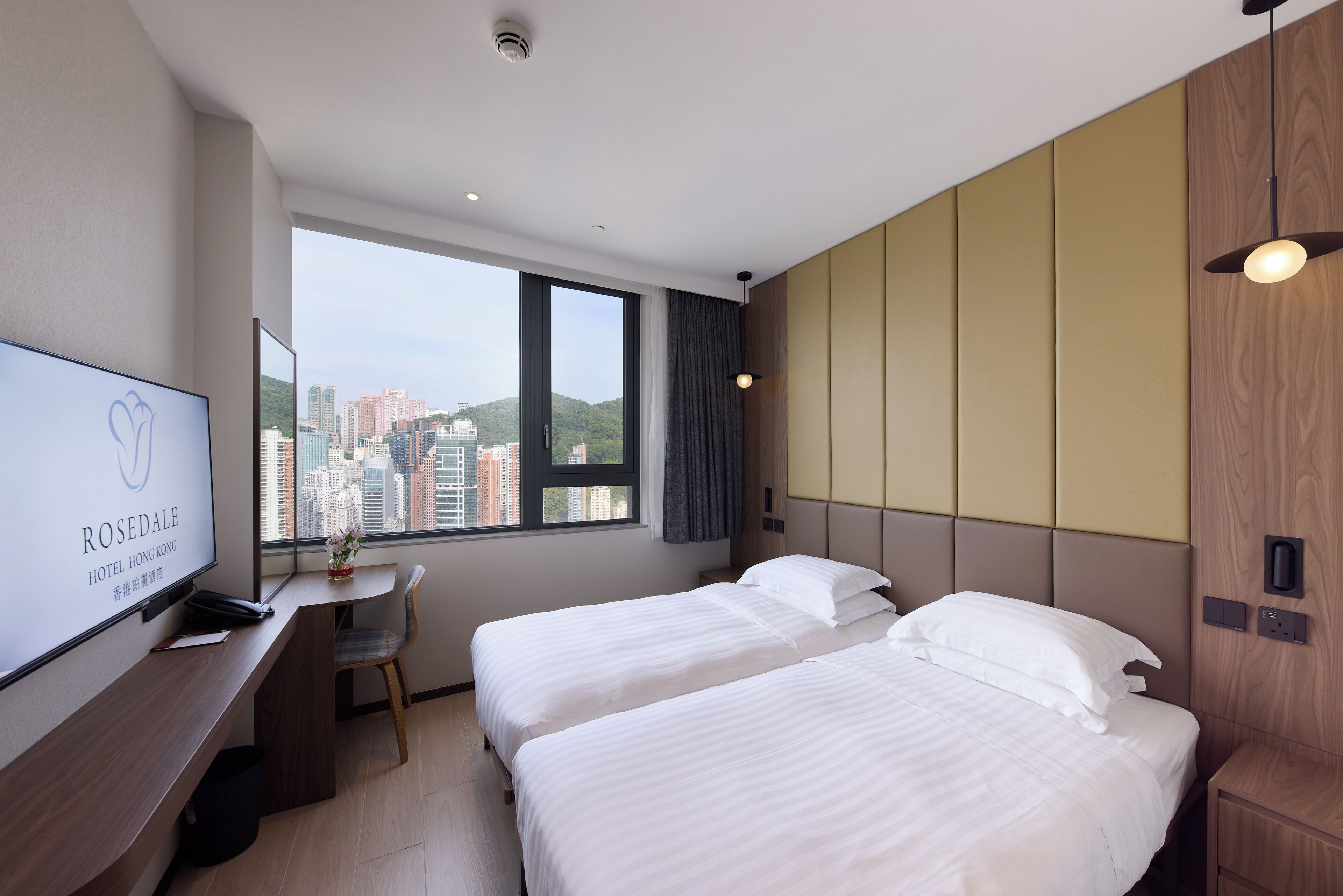 Habitación de hotel con dos camas, un escritorio, un televisor y una ventana con vistas a la ciudad.