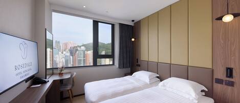 Habitación de hotel con dos camas, un escritorio, un televisor y una ventana con vistas a la ciudad.