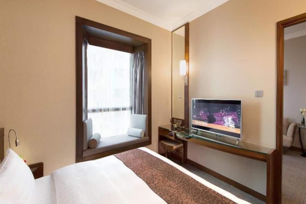 A hotel room with a large bed, a desk with a computer, a TV on the wall, and a window with a view.
