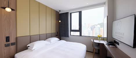 A hotel room with a large bed, a desk with a chair, a TV, and a window with a city view.