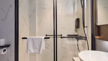 Un baño moderno con ducha de vidrio, lavamanos blanco y paredes de mármol.