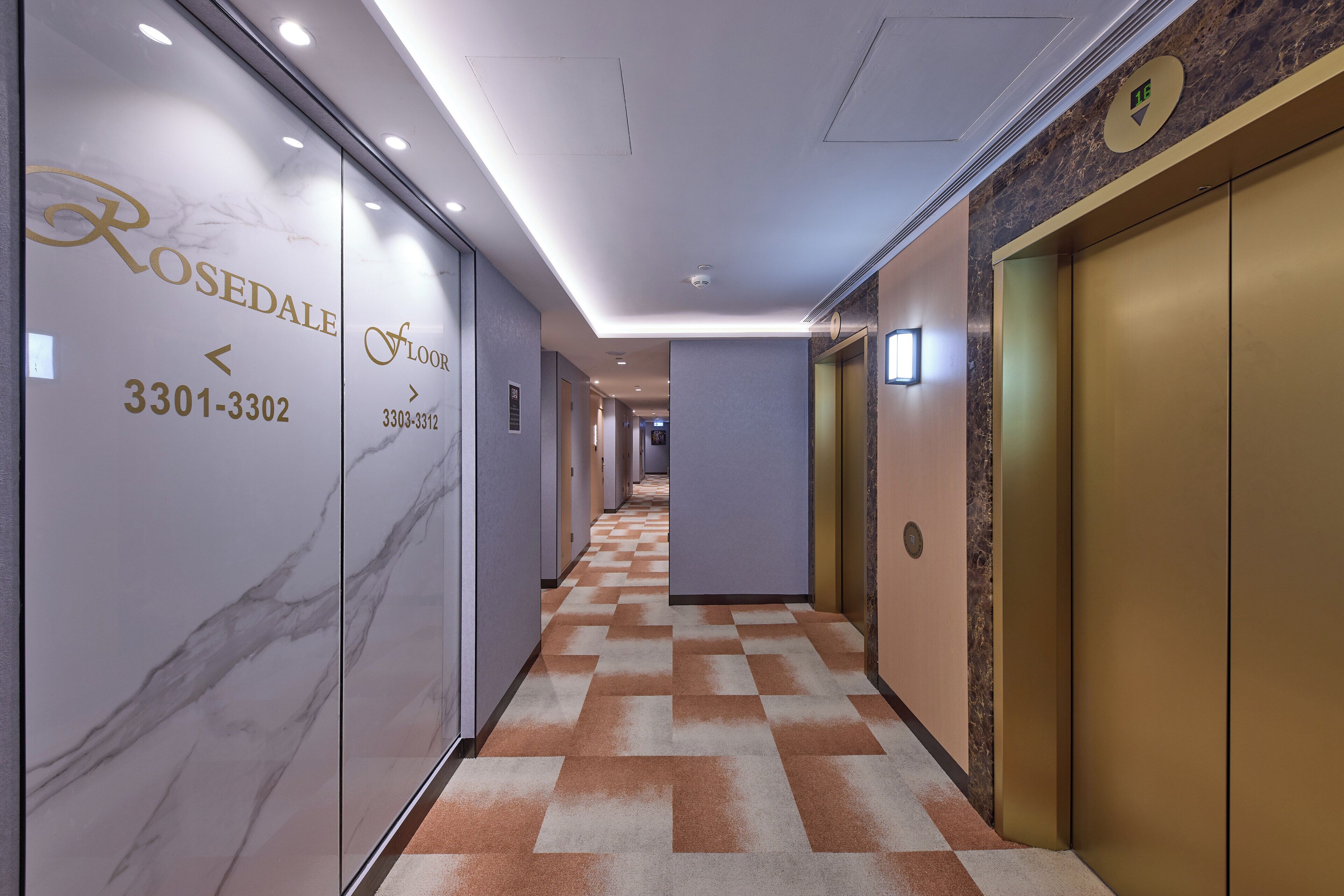 A hotel corridor with marble walls, checkered carpet, and gold elevators.