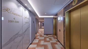 A hotel corridor with marble walls, checkered carpet, and gold elevators.
