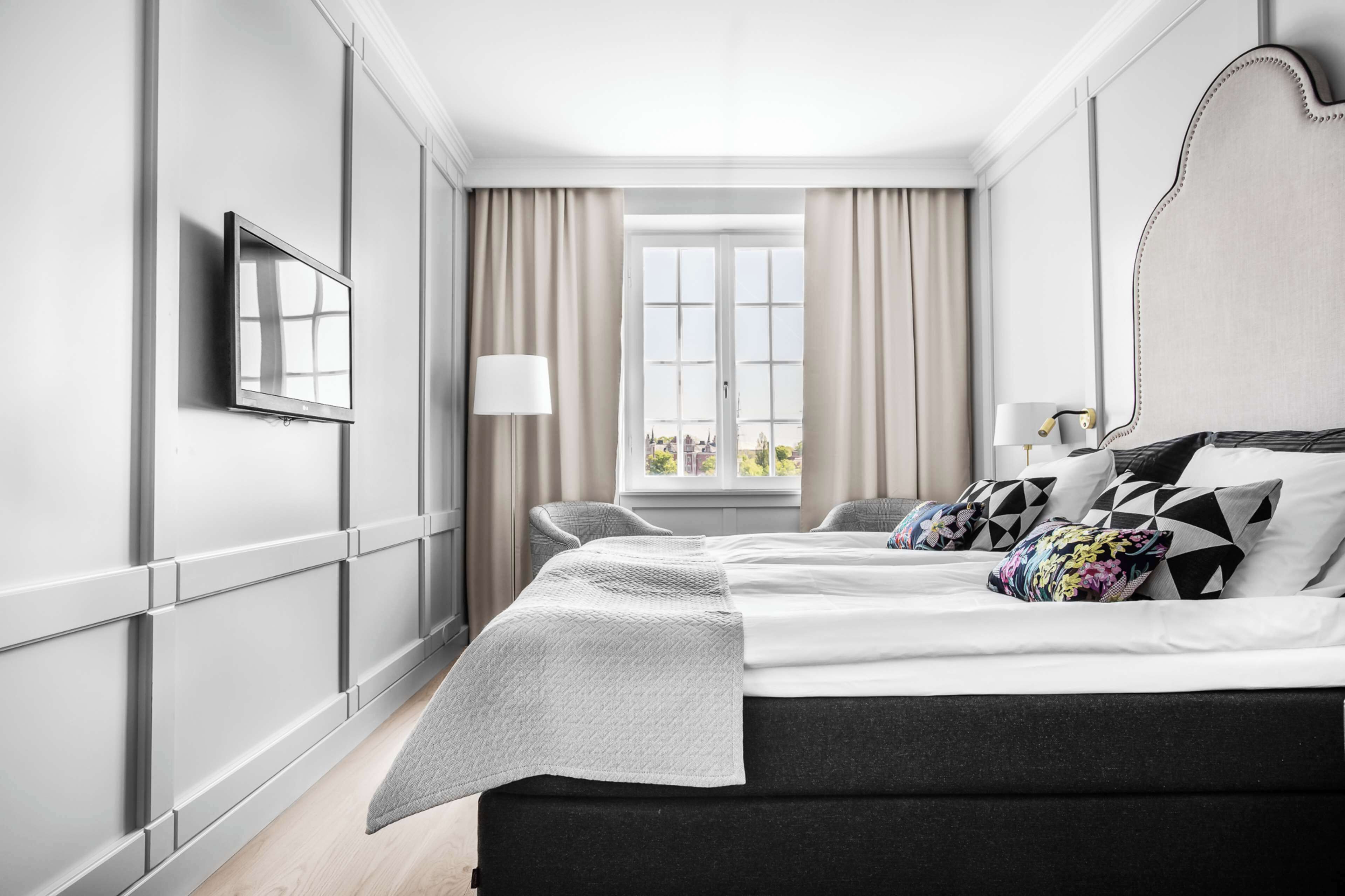 Una habitación de hotel moderna con una cama grande, televisión, ventana con cortinas y vistas a la ciudad.