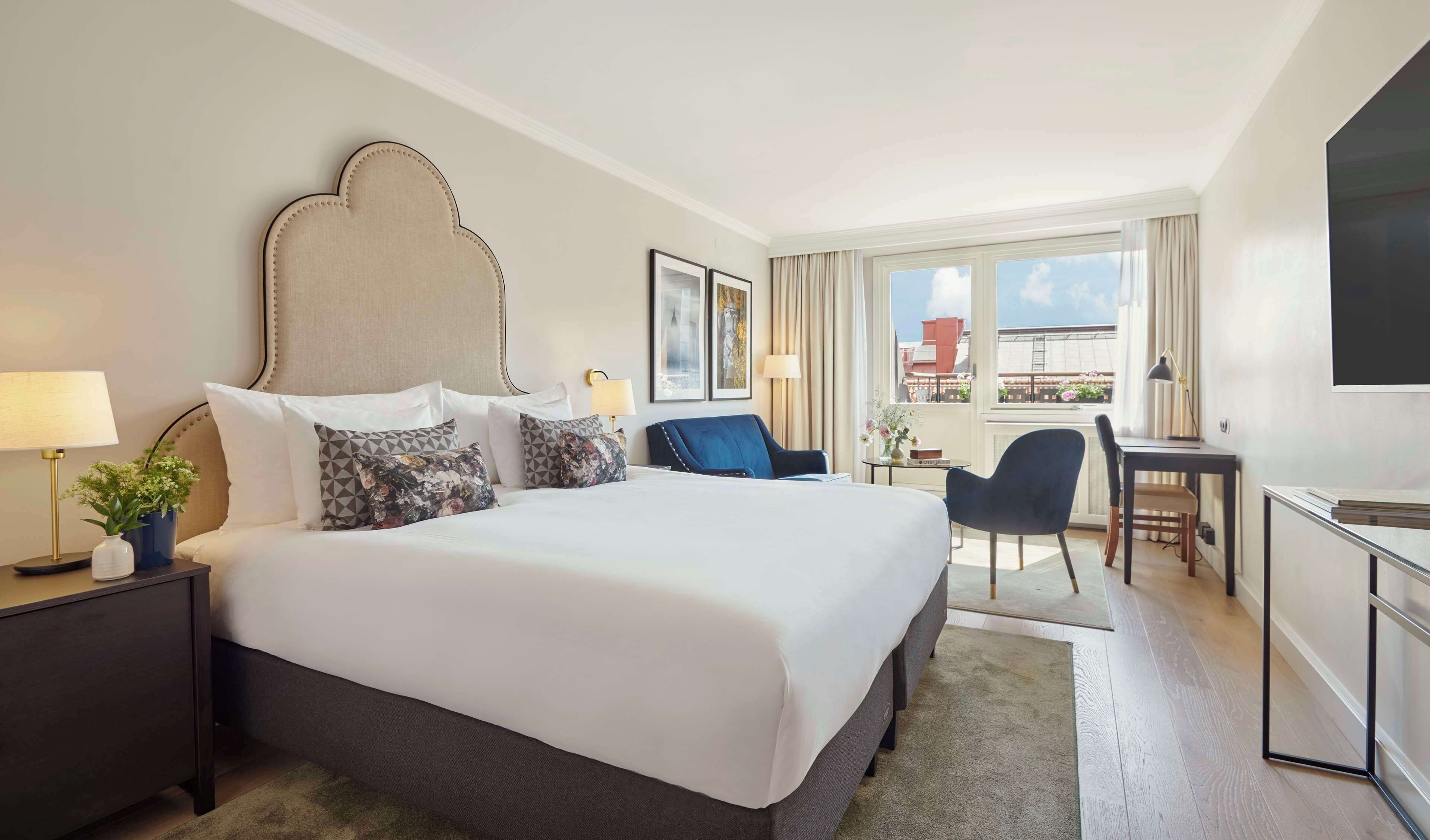 A hotel room with a large bed, a desk, a chair, and a TV.