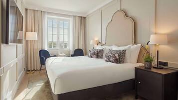 Ett hotellrum med en stor säng, två sänglampor, ett skrivbord med en lampa, en stol och utsikt över staden genom fönstret.
