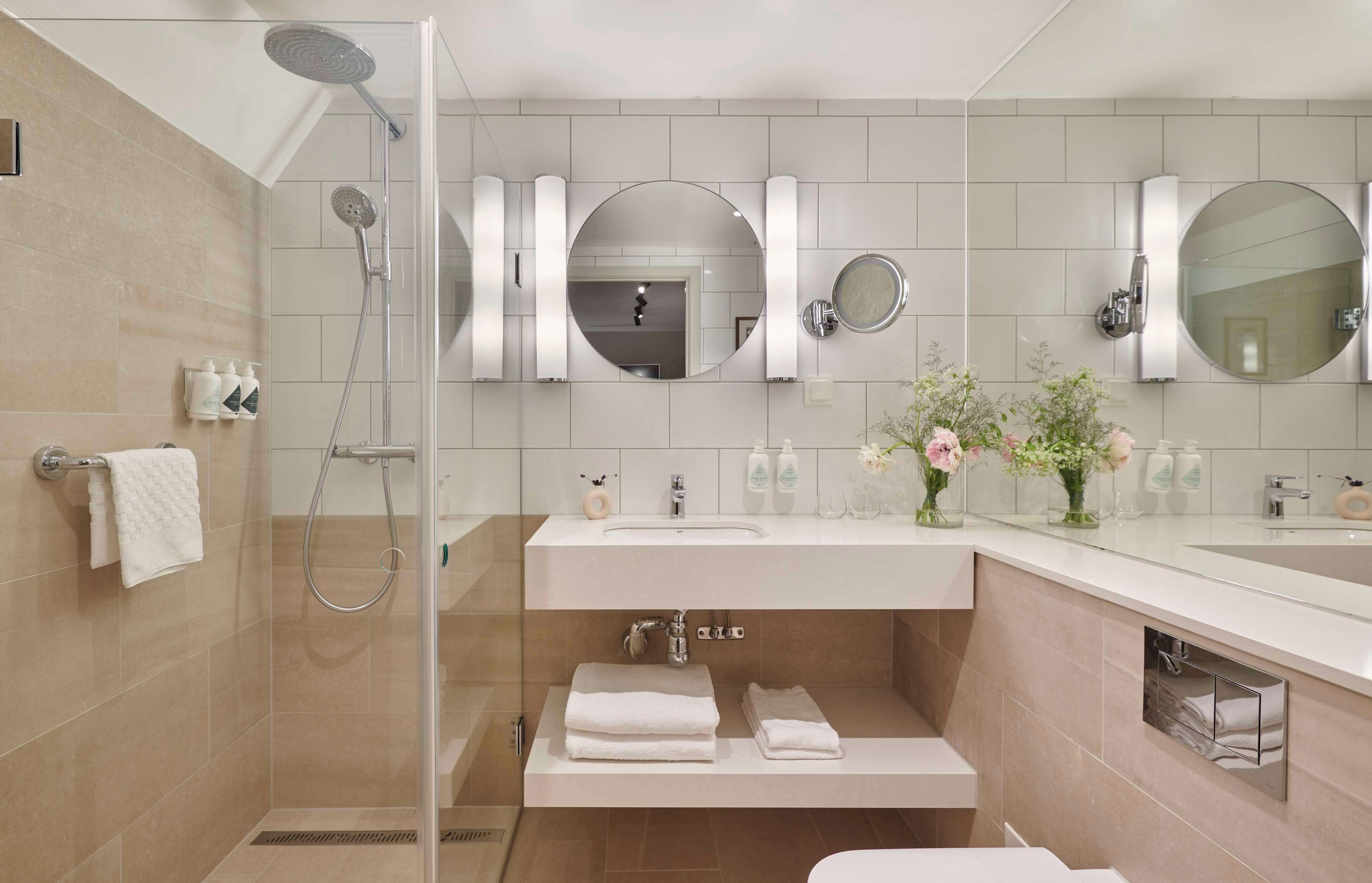 Un baño moderno con ducha de vidrio, tocador con lavamanos y dos espejos.