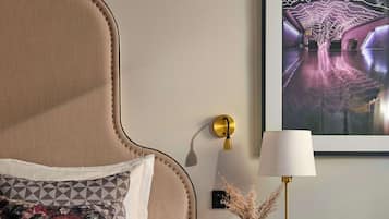 A bedroom with a large bed, a nightstand, a lamp, a framed picture, and a wall-mounted light.