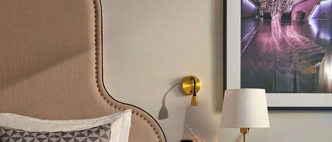 A bedroom with a large bed, a nightstand, a lamp, a framed picture, and a wall-mounted light.
