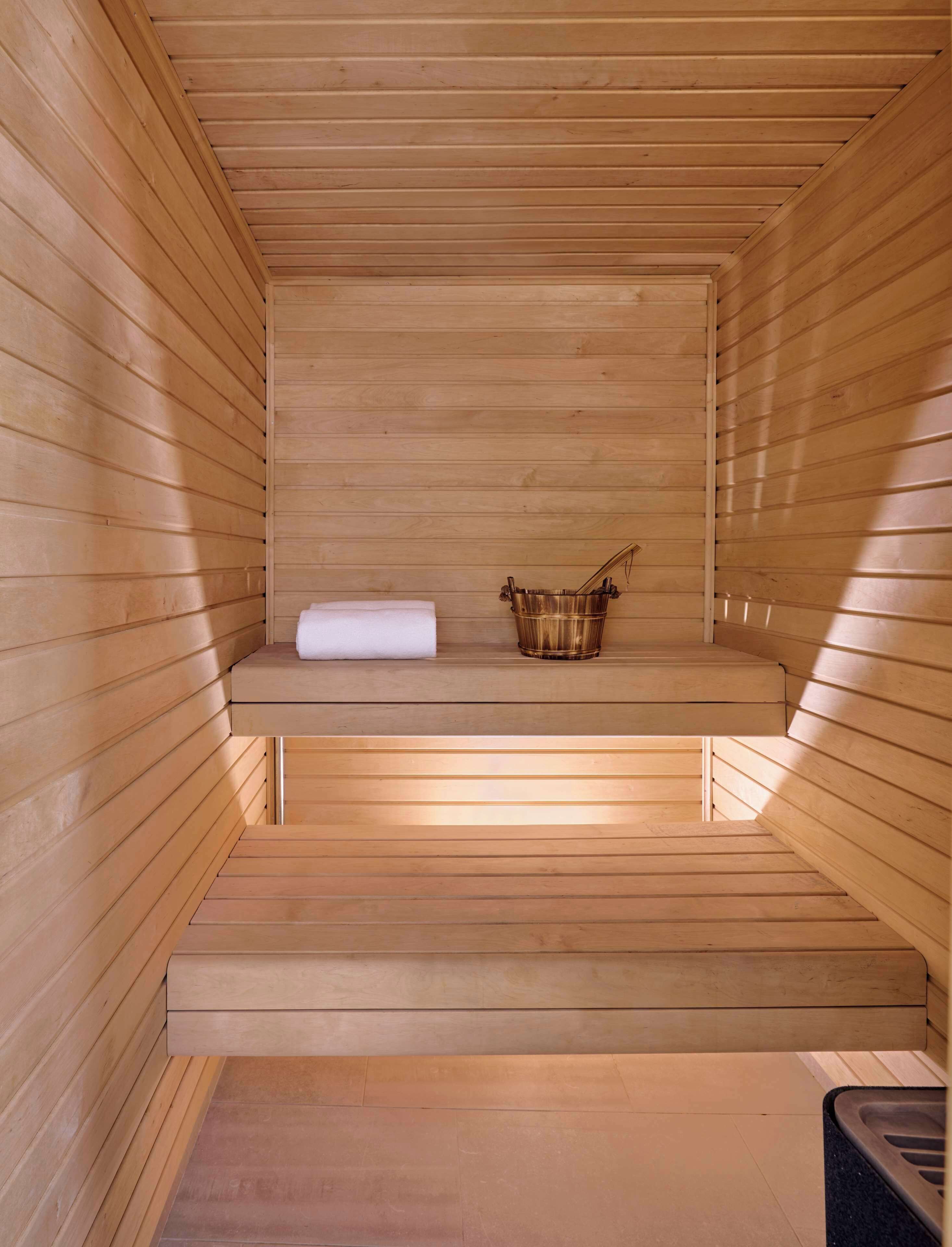 Una sala de sauna con paredes y bancos de madera, una toalla y un balde.