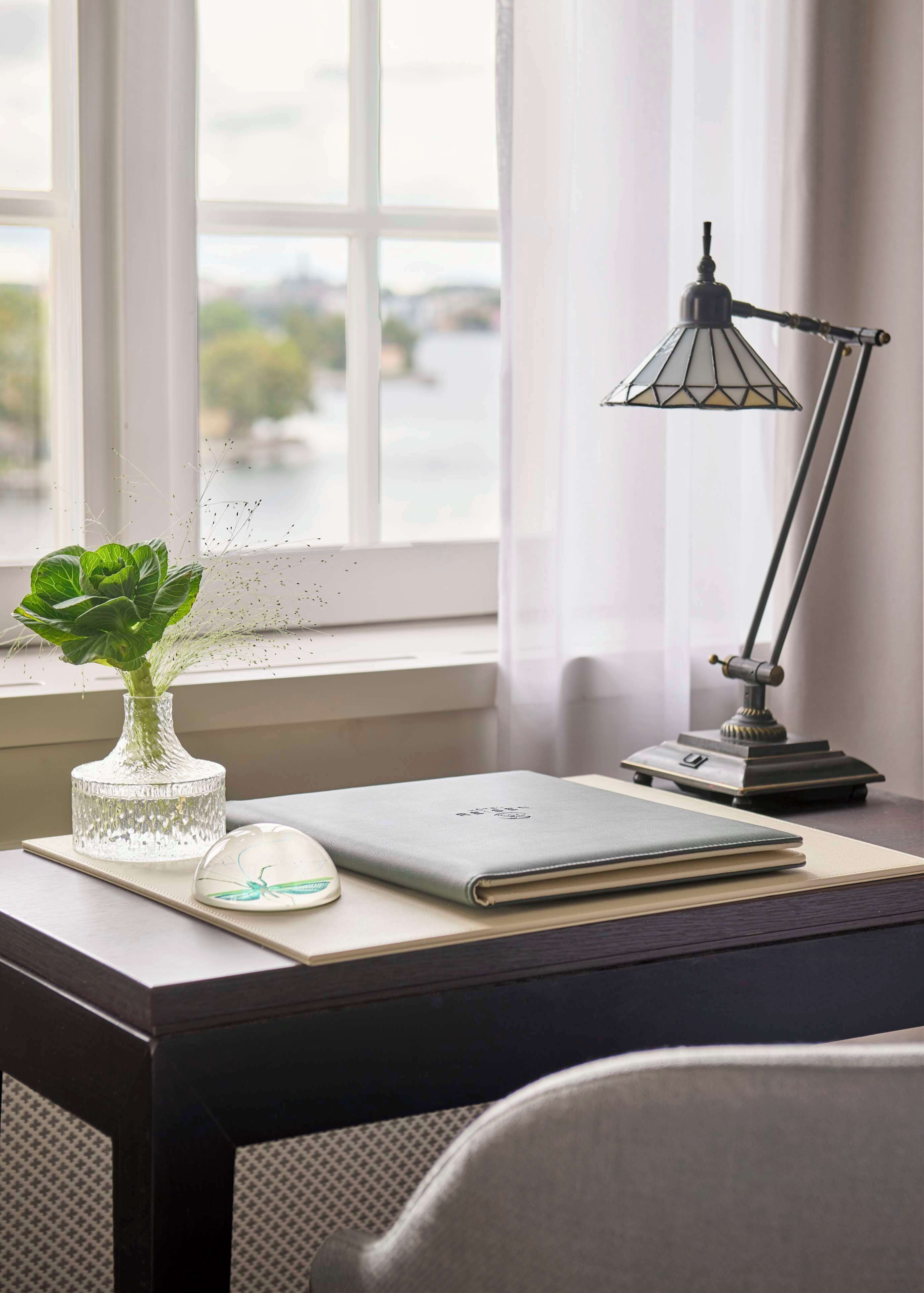 Un bureau avec un ordinateur portable, un vase avec une plante, une souris et une lampe de bureau.