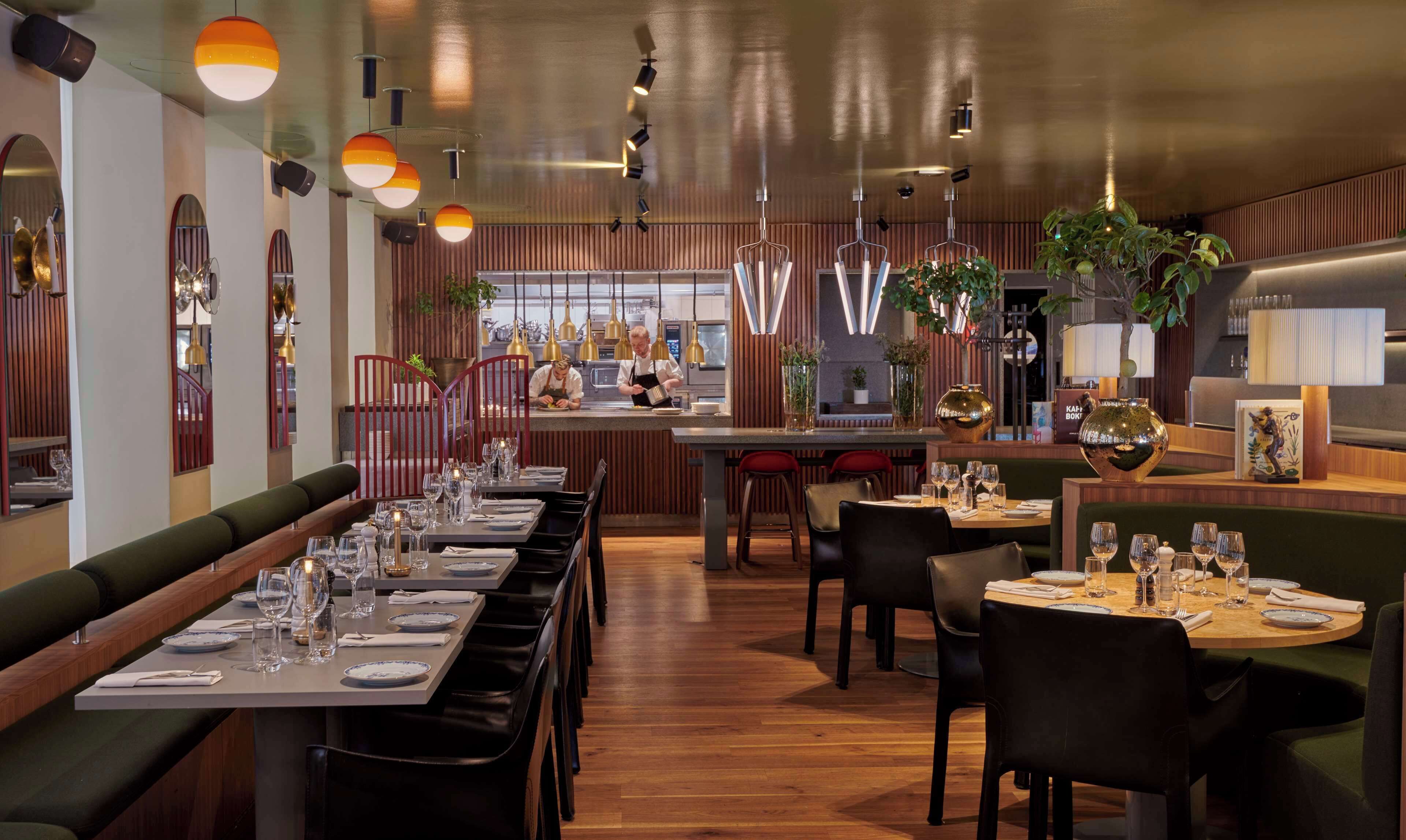 A restaurant interior with long communal tables, individual booths, and a bar area.