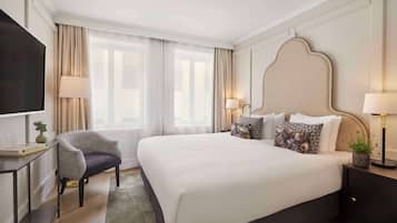 Une chambre d’hôtel avec un grand lit, deux tables de chevet avec des lampes, une chaise, un téléviseur et une fenêtre avec des rideaux.