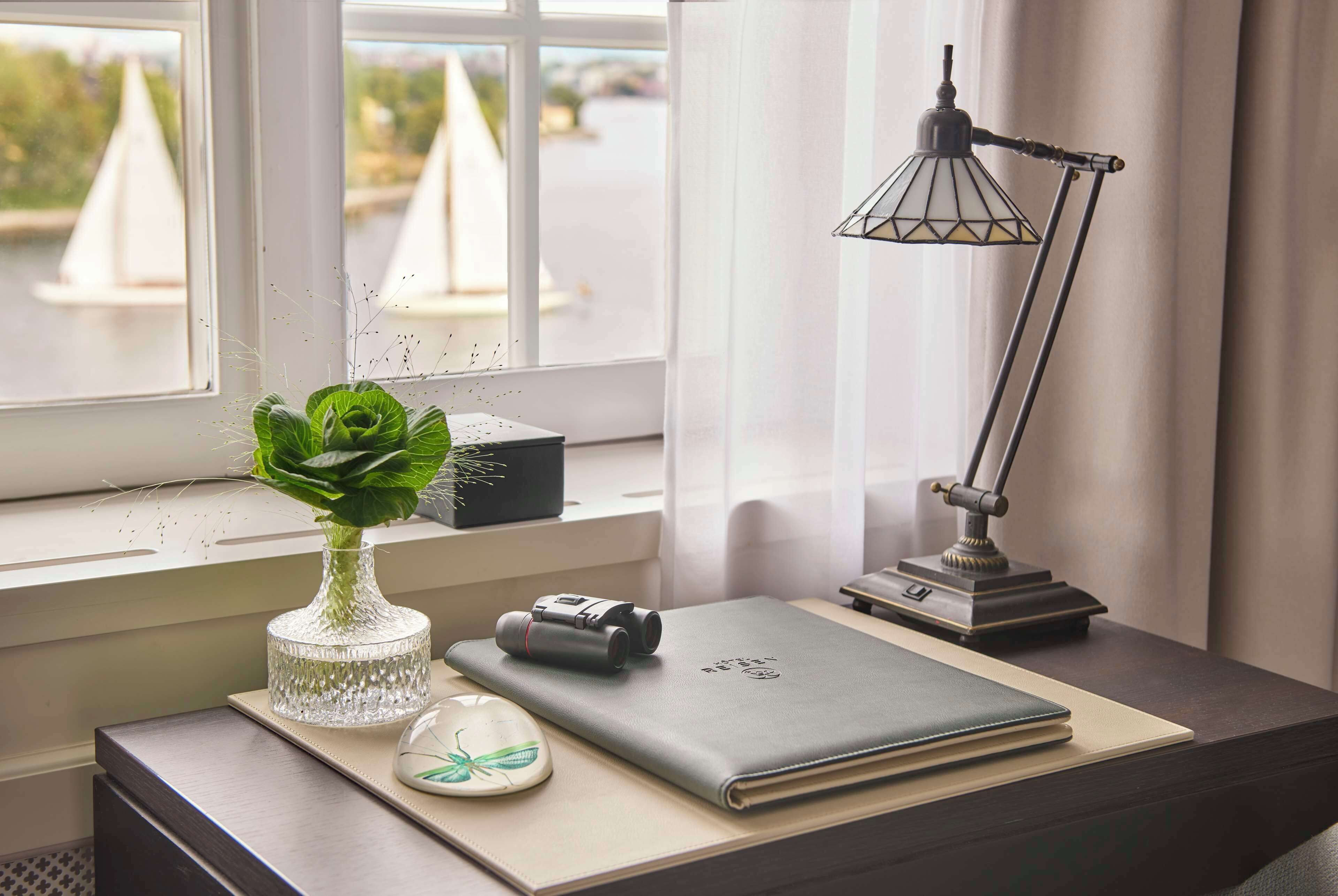 Un escritorio con una computadora portátil, una cámara, un florero con una planta y una lámpara.
