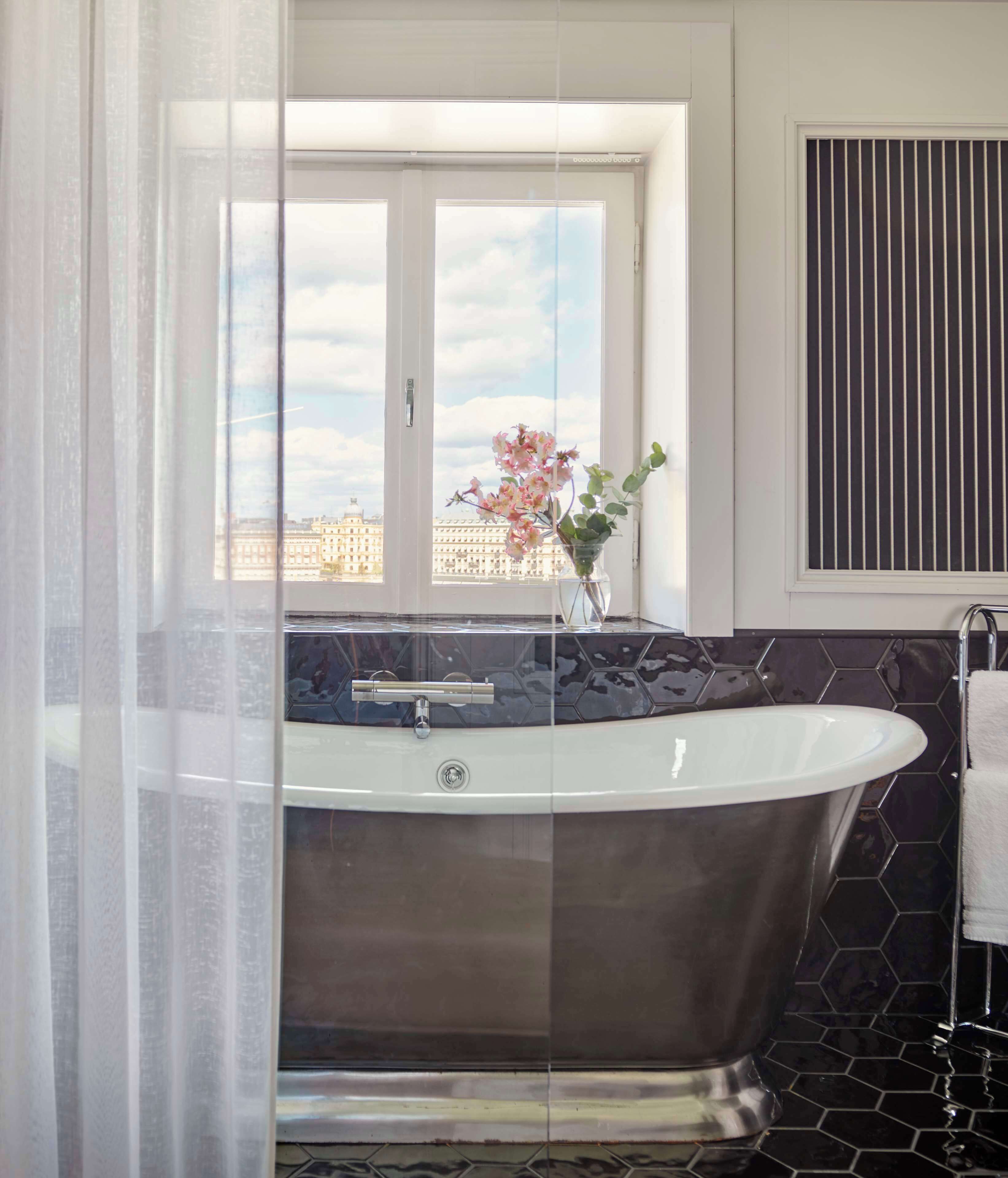 Un baño moderno con una bañera independiente, un ventanal con vistas a la ciudad y un suelo de baldosas blanco y negro.