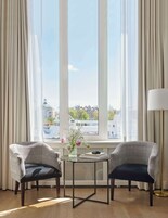 Una habitación con dos sillones, una mesita y una ventana que ofrece vistas a edificios y un barco.
