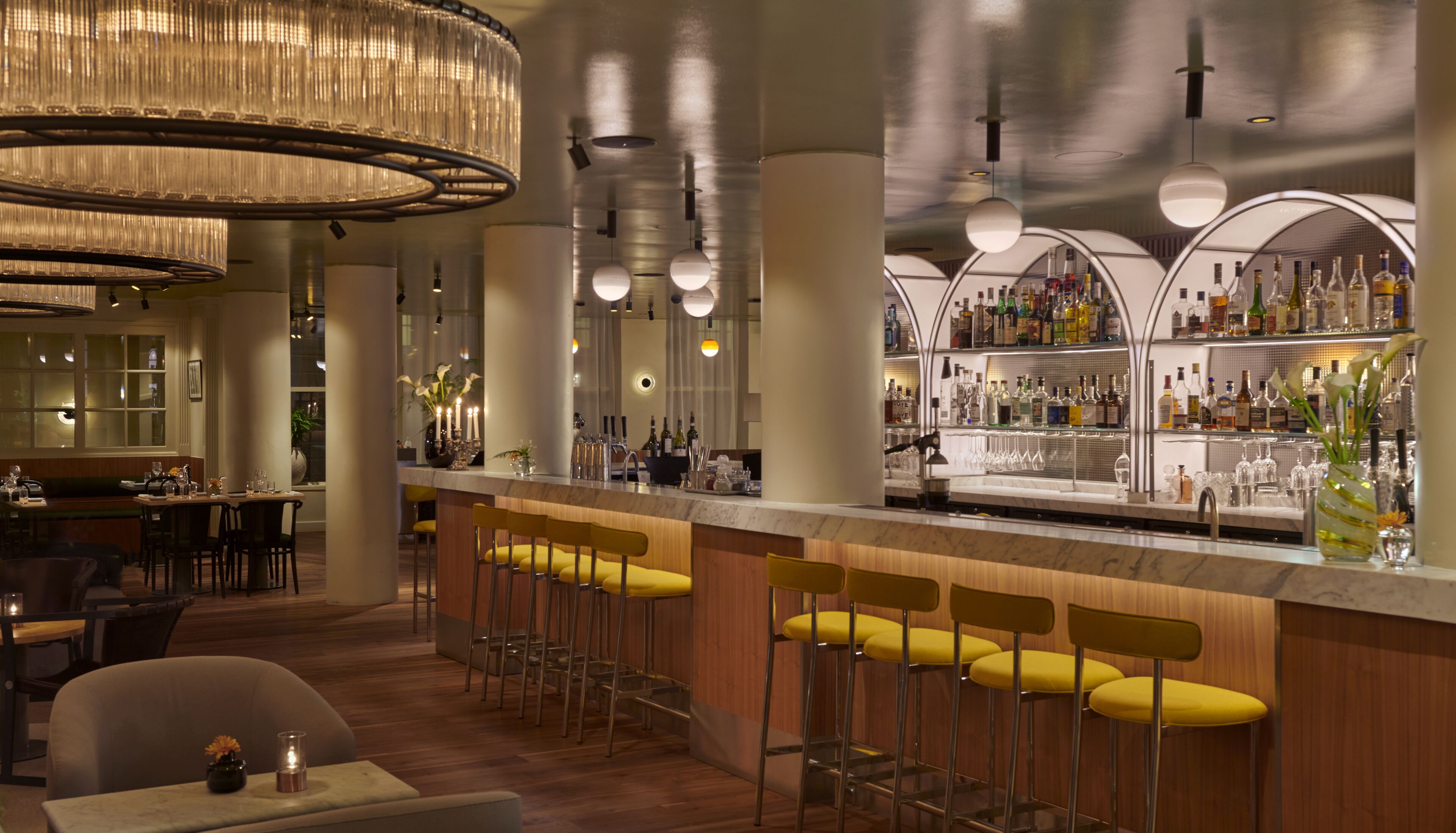 A bar area with high stools, a bar counter, and a variety of bottles and glasses.