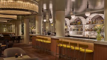 A bar area with high stools, a bar counter, and a variety of bottles and glasses.