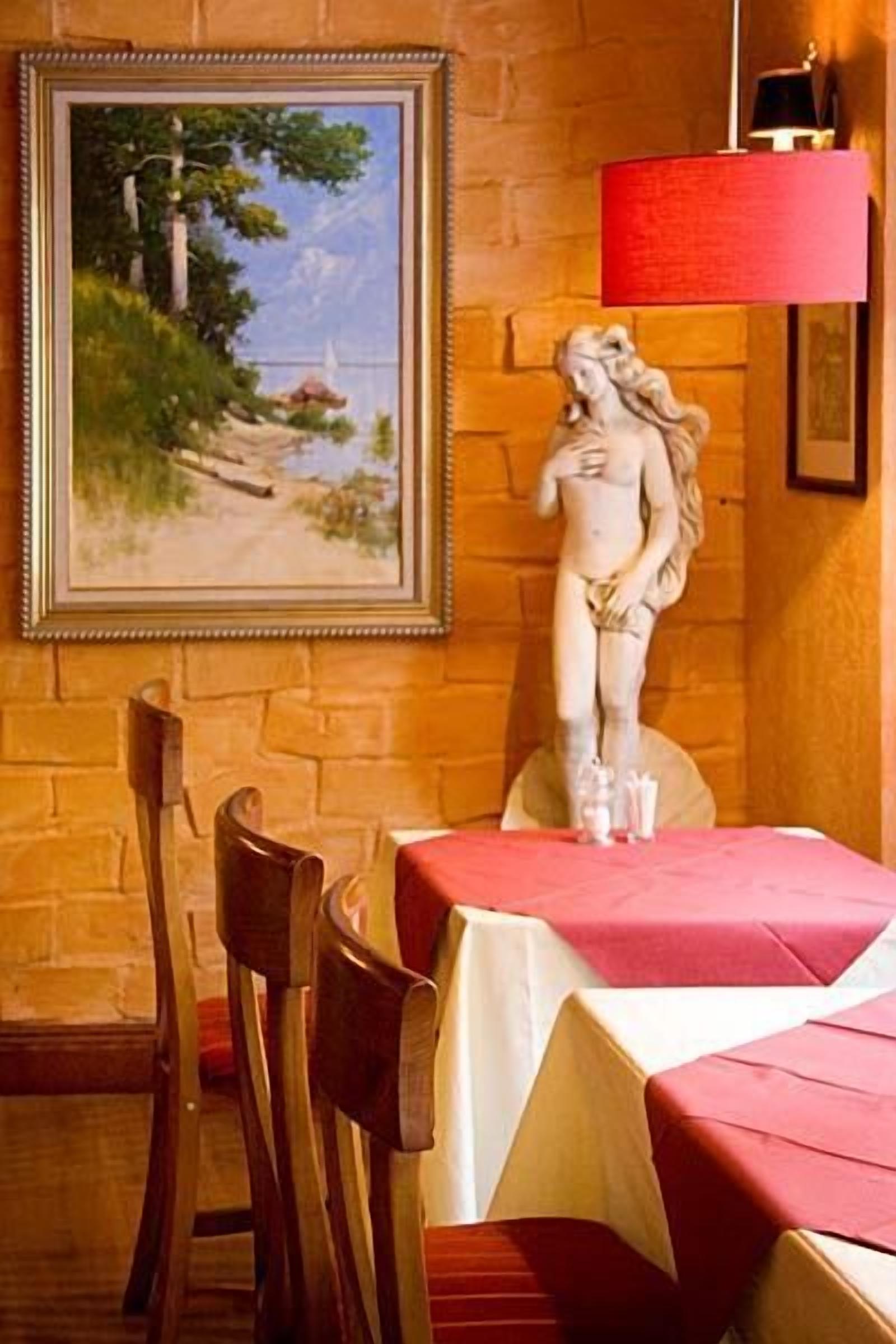 Un comedor con una mesa lista para dos personas, una estatua y un cuadro en la pared.