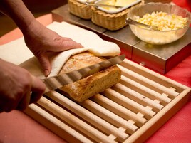 Uma pessoa cortando uma gaveta de pão em uma tábua de corte de madeira.