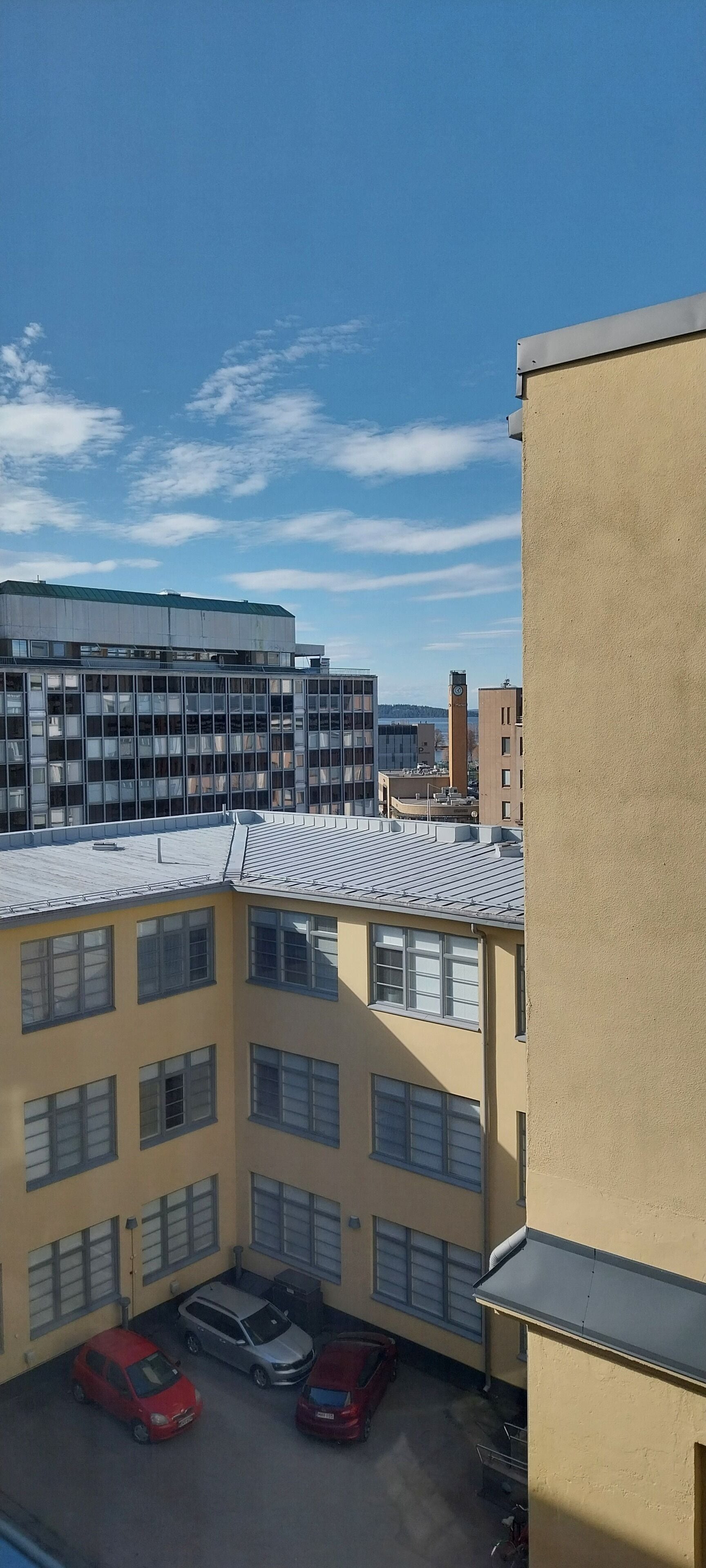 Un edificio de varios pisos con techo plano y ventanas amplias. Hay varios coches estacionados al frente.