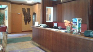 A reception area with a wooden reception desk, a mirror, a vase with flowers, and a small plant. - Kauppahotelli (Lahti)