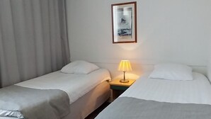 A hotel room with two single beds, a nightstand with a lamp, and a framed picture on the wall. - Kauppahotelli (Lahti)