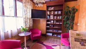 A cozy room with a flat-screen TV, a bookshelf with books and magazines, a potted plant, and two pink armchairs. - Kauppahotelli (Lahti)