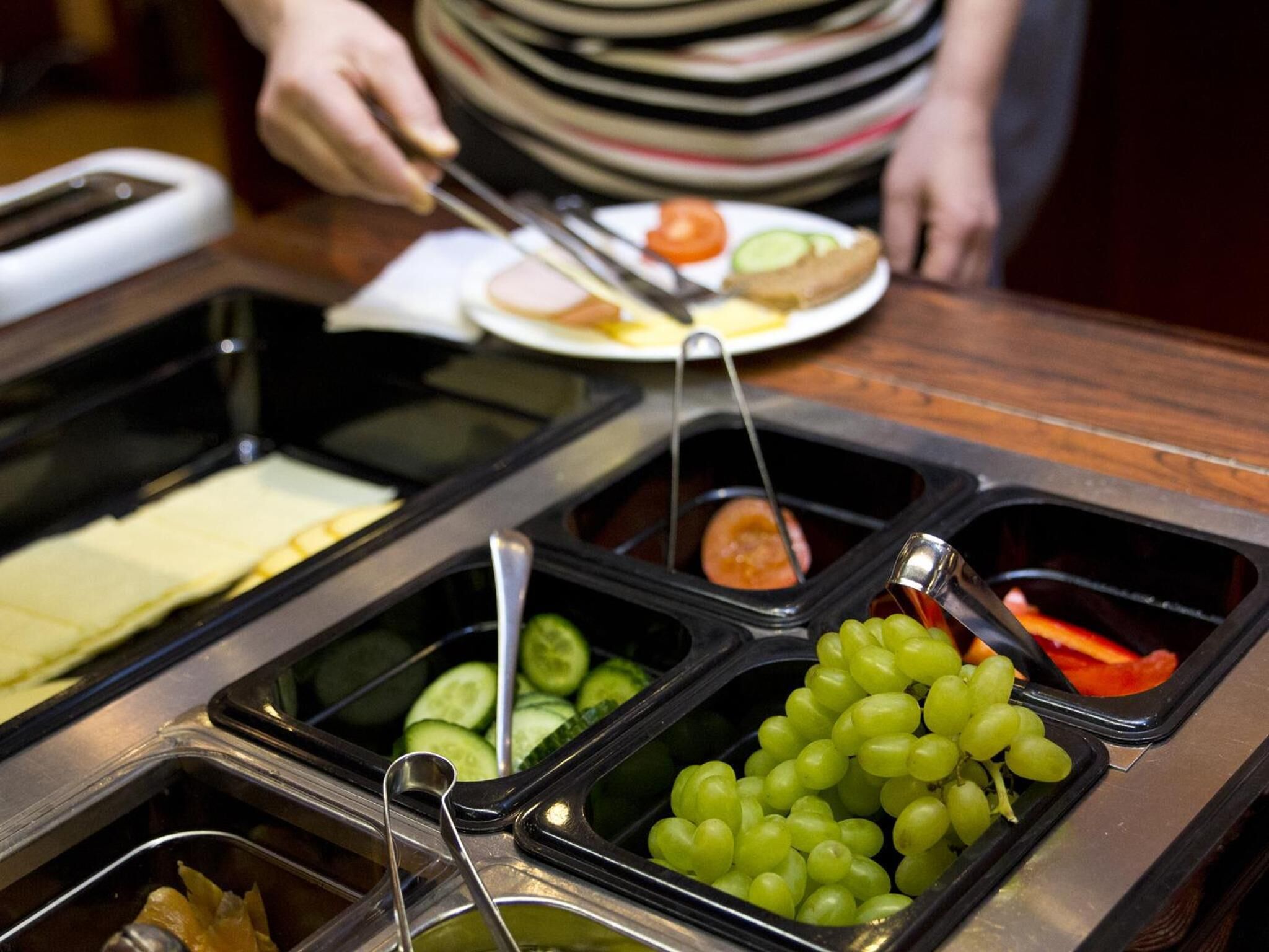 A buffet with various food options including sliced cucumbers, grapes, and a plate with a sandwich and a small tomato.