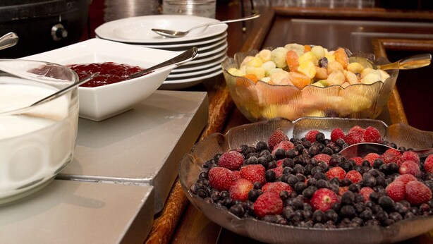 A buffet setup with various food items, including fruits and a bowl of yogurt. - Kauppahotelli (Lahti)