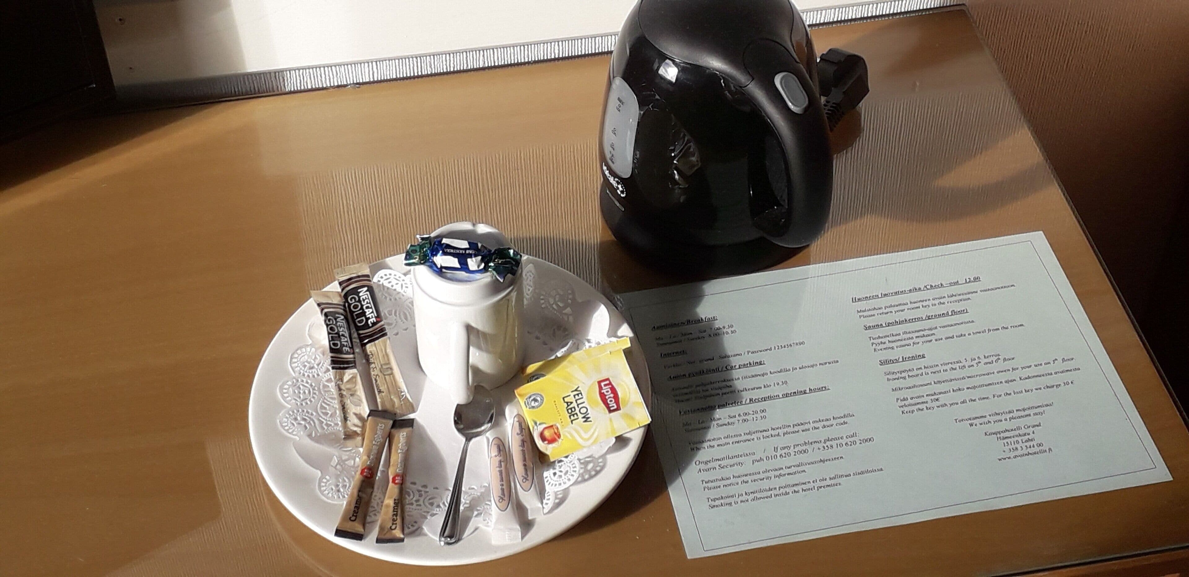 A table with a plate of food, a spoon, a packet of Luno, and a black object, possibly a mouse, next to a menu.