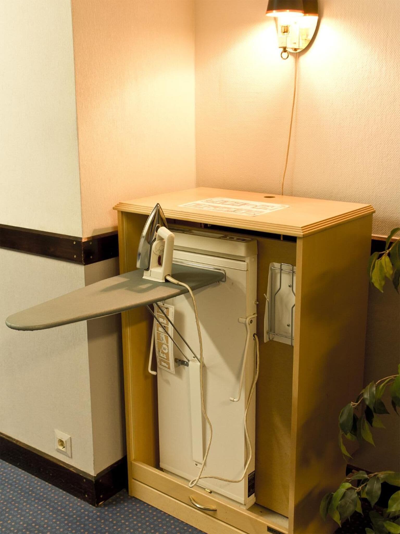 A compact room with a small desk, a chair, a desk lamp, and a potted plant.