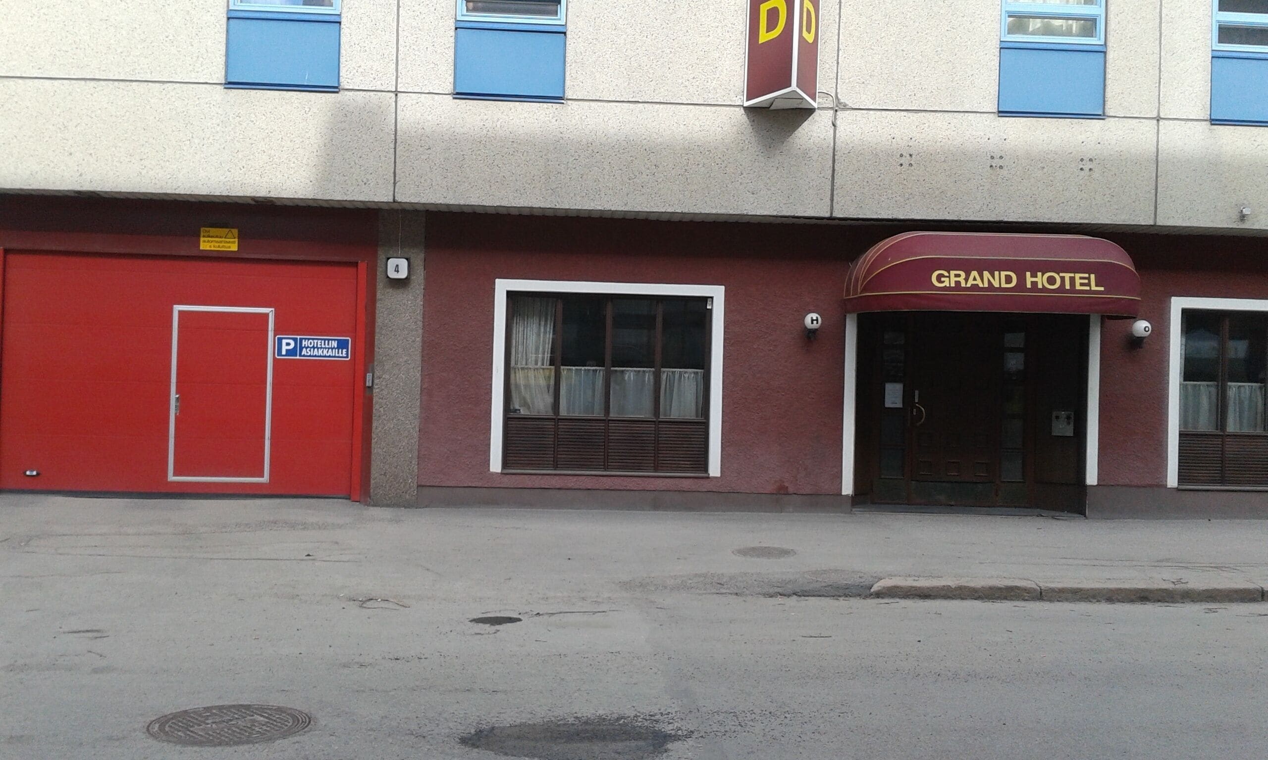 A building with a red door labeled "HOTELLIN ASIAKAILLE" and a sign for "GRAND HOTEL" above the entrance.