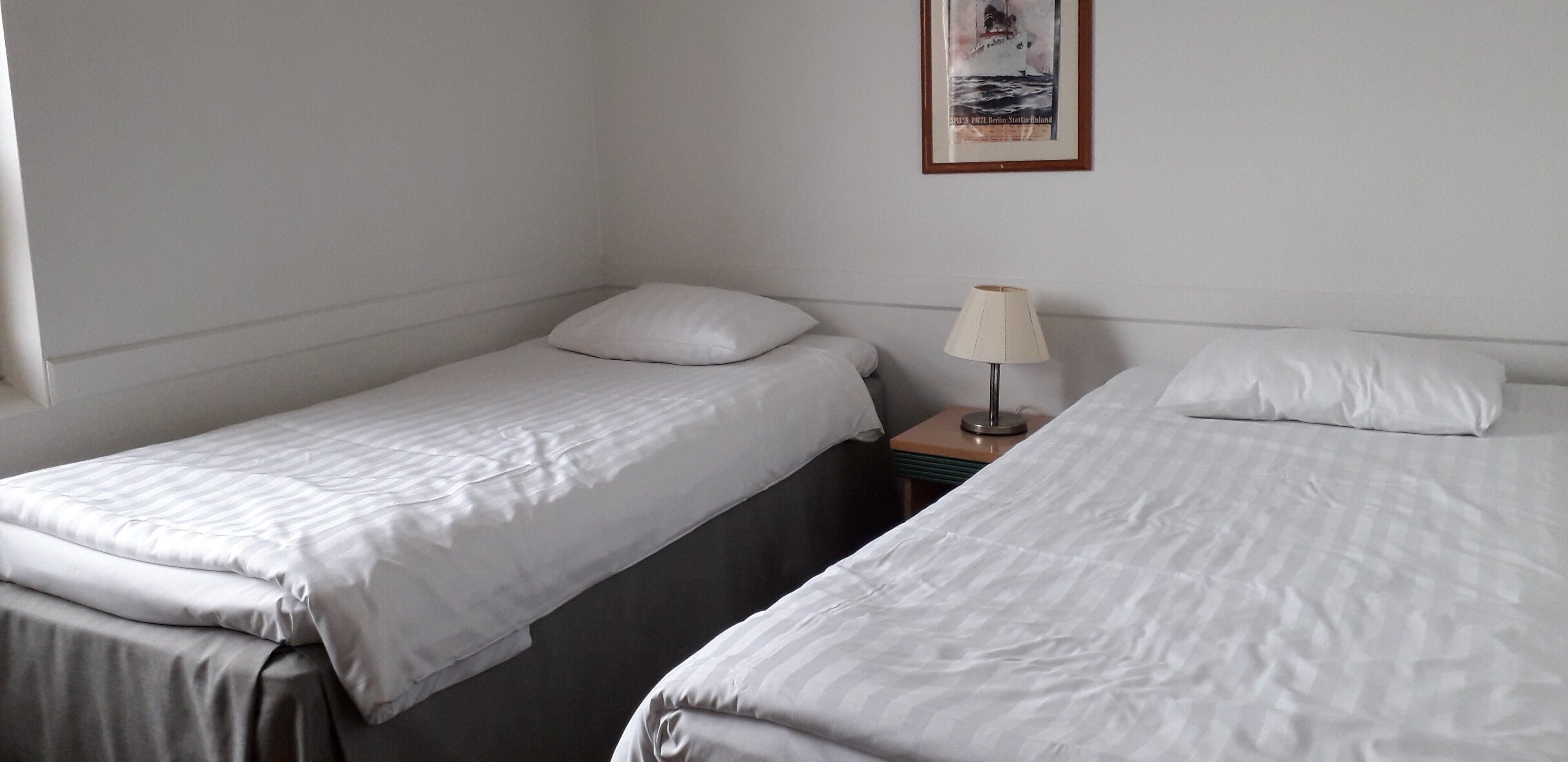 A simple room with two single beds, a nightstand with a lamp, and a framed picture on the wall.