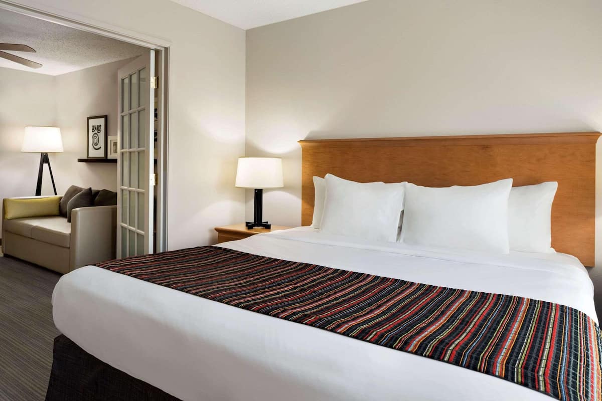A hotel room with a large bed, a bedside table with a lamp, a sofa, and a door leading to another room.