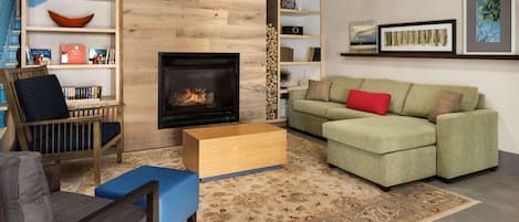 A living room with a fireplace, green sofa, blue ottoman, and a bookshelf.