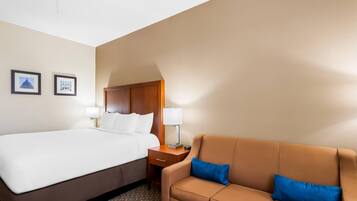 A hotel room with a bed, a brown sofa, two wall-mounted lamps, and framed pictures on the wall.