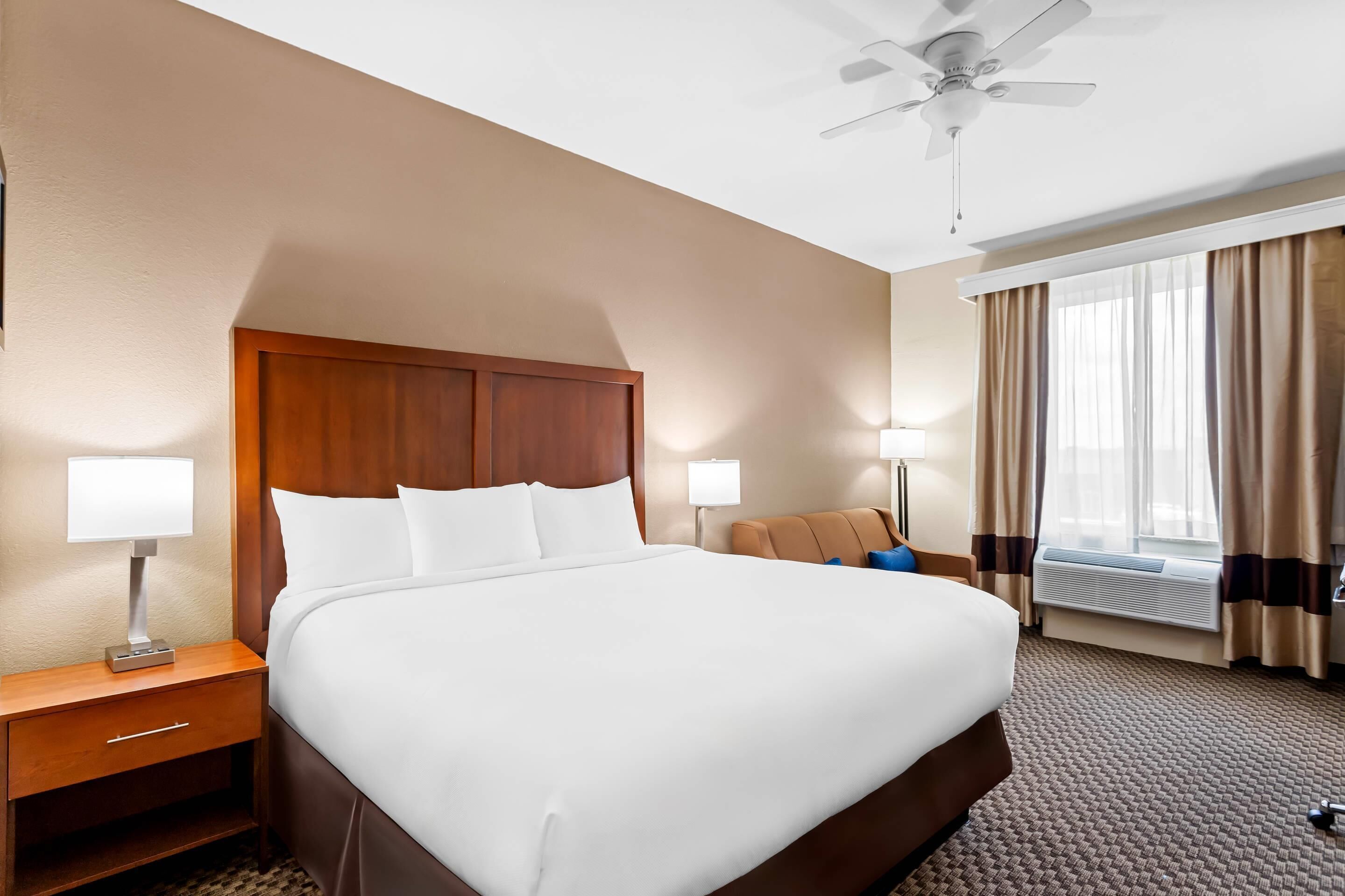 Une chambre d’hôtel avec un grand lit, des tables de chevet avec des lampes, un ventilateur de plafond et une fenêtre avec des rideaux.