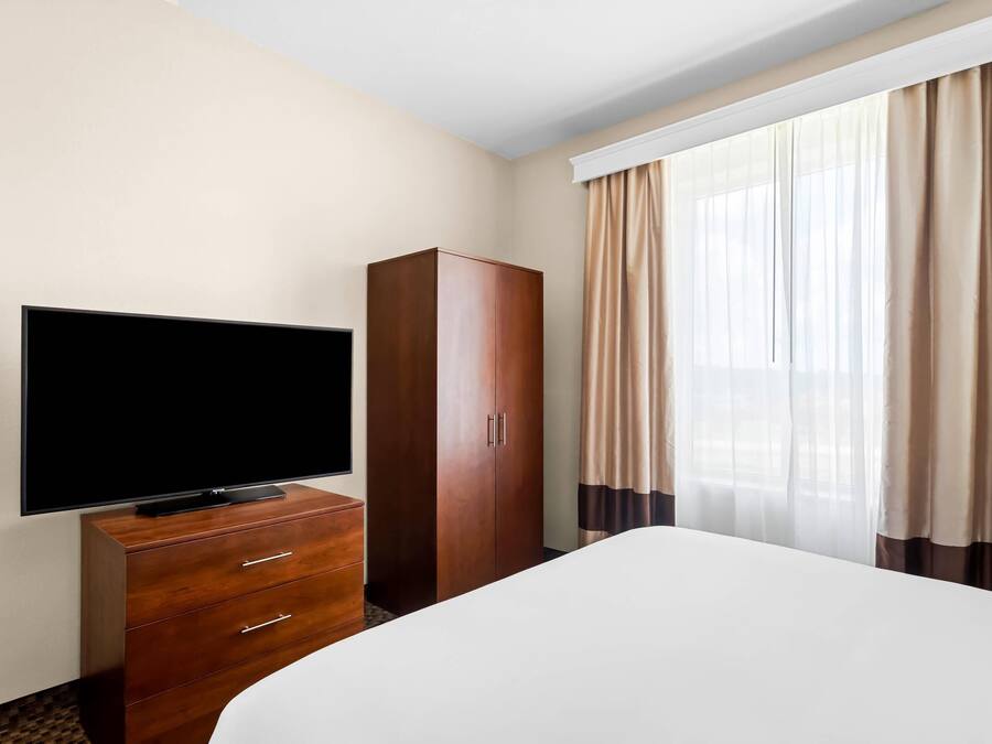 A hotel room with a bed, a TV on a wooden dresser, a wardrobe, and a window with curtains.