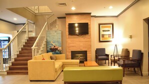A living room with a staircase, a fireplace, a flat-screen TV, and a painting on the wall. - Sonesta Essential IAH Airport JFK Boulevard (Houston)