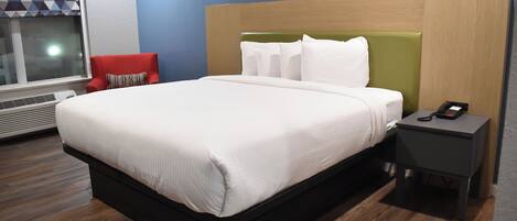 Una habitación de hotel moderna con una cama grande, una silla roja, una mesita de noche con un teléfono y una ventana con una persiana de diseño geométrico.