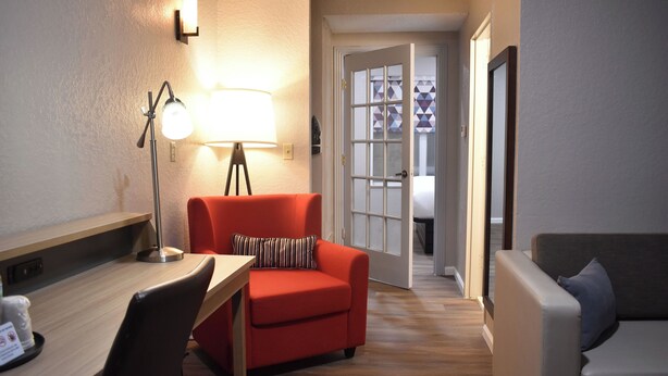A room with a wooden desk, a red sofa, a grey sofa, and a lamp. - Sonesta Essential IAH Airport JFK Boulevard (Houston)