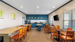 A modern kitchen with blue cabinets, a central island, and a dining area with wooden tables and chairs. - Sonesta Essential IAH Airport JFK Boulevard (Houston)