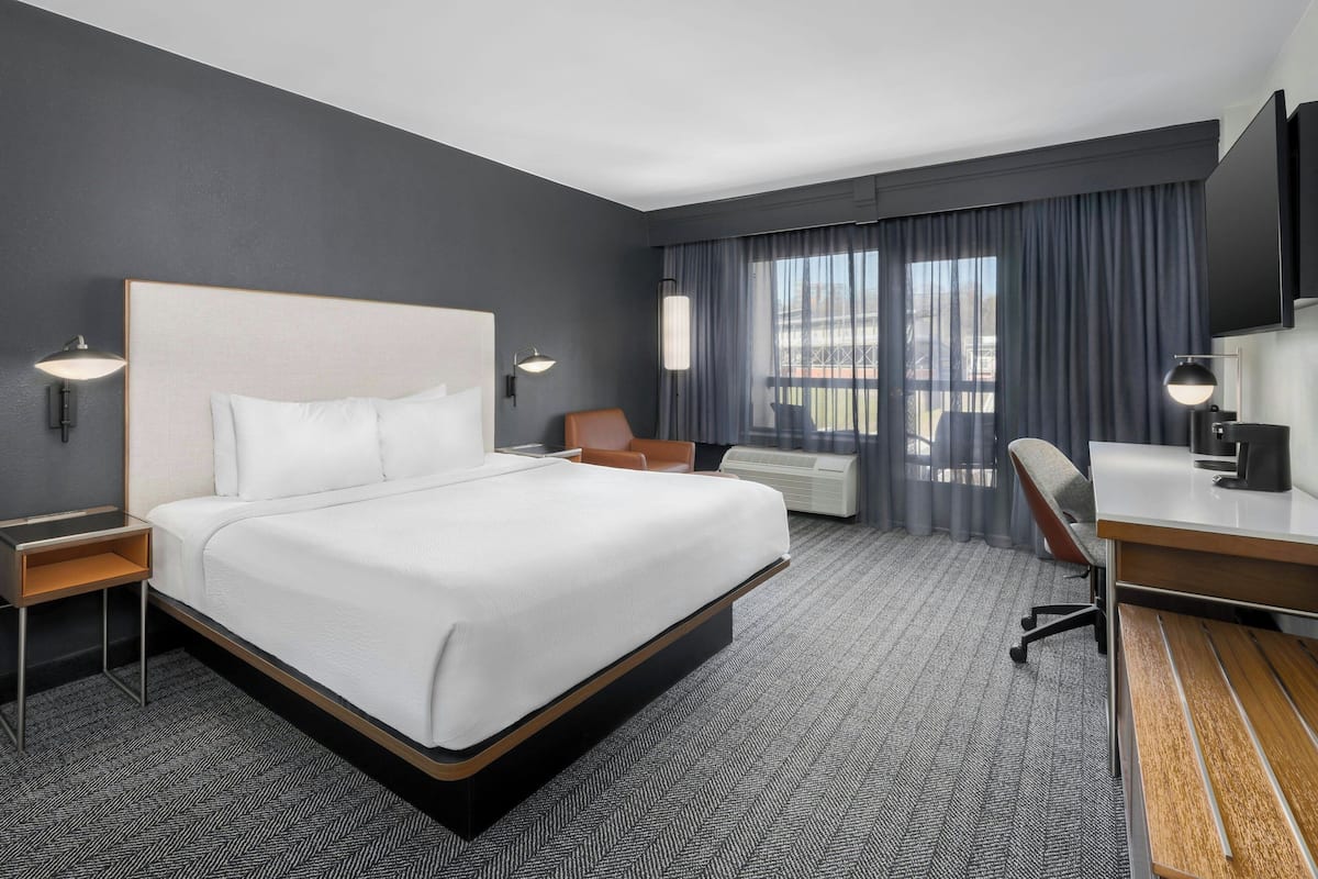 A modern hotel room with a large bed, a desk, a chair, and a TV.