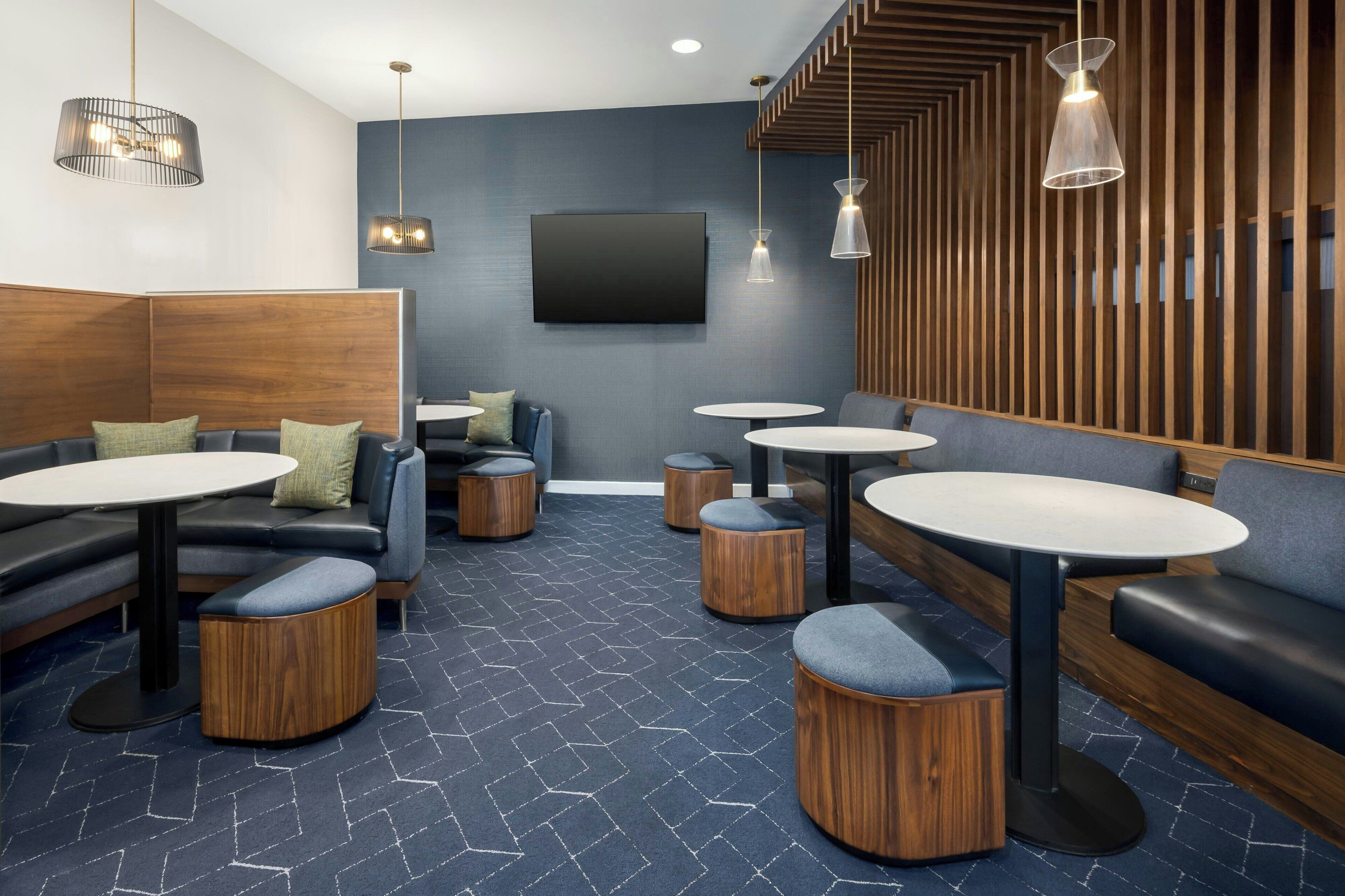 A modern lounge area with round tables, cushioned seating, and a large TV screen.