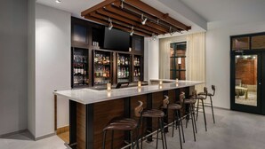 A modern bar area with a long counter, multiple stools, and a variety of bottles and glasses. - Courtyard by Marriott Chattanooga Downtown (Chattanooga)