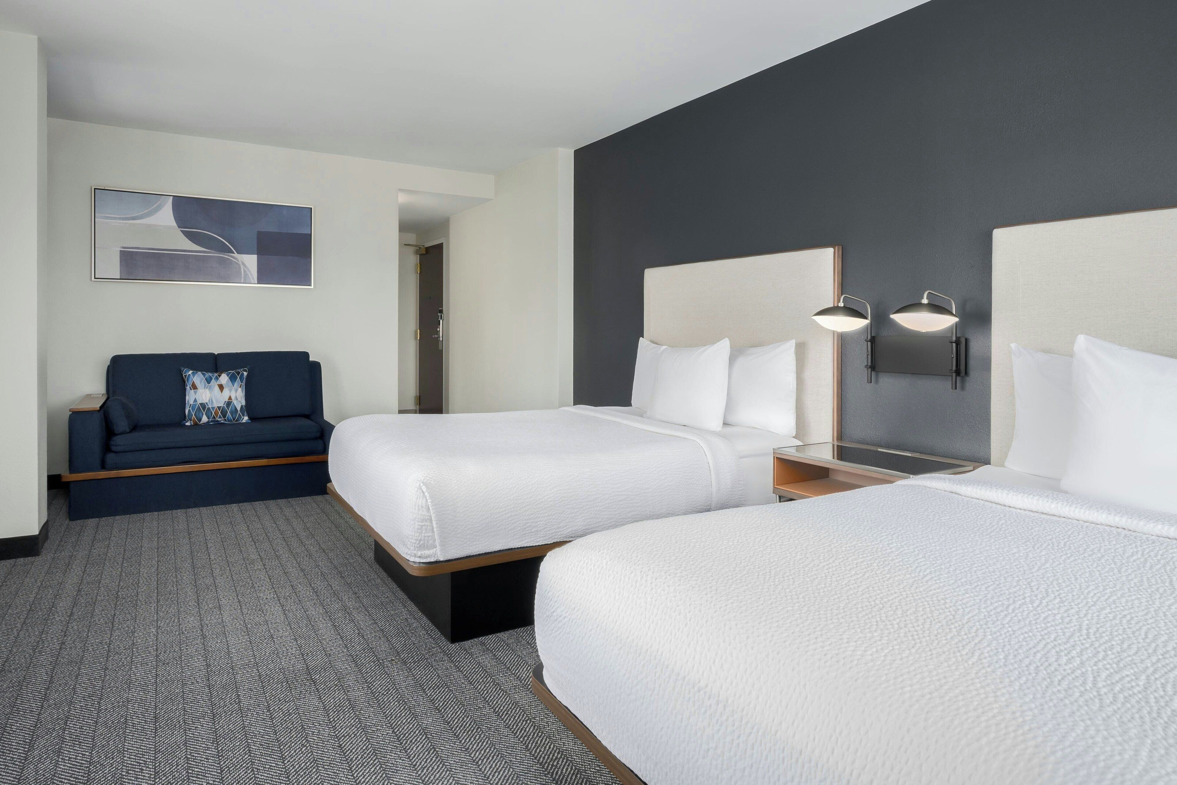 A hotel room with two beds, a sofa, and a painting on the wall.