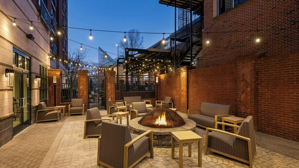 An outdoor patio with wicker furniture, a central fire pit, and string lights. - Courtyard by Marriott Chattanooga Downtown (Chattanooga)